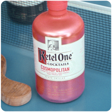 Ketel One pre-mixed cosmopolitan cocktail on a table next to a cutting board